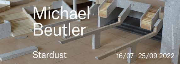 Das Banner zur Ausstellung Michael Beutler. Stardust. Im Hintergrund ist ein von ihm gebautes Modell des Wilhelm-Hack-Museums aus Holz und selbst geschöpftem Papier. In weißer Schrift steht der Titel und der Ausstellungszeitraum: 16.7-25.9.2022